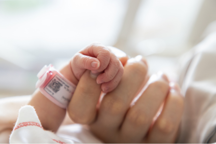 a close-up of a newborn infant baby's tiny hand wrapped around their mother's finger