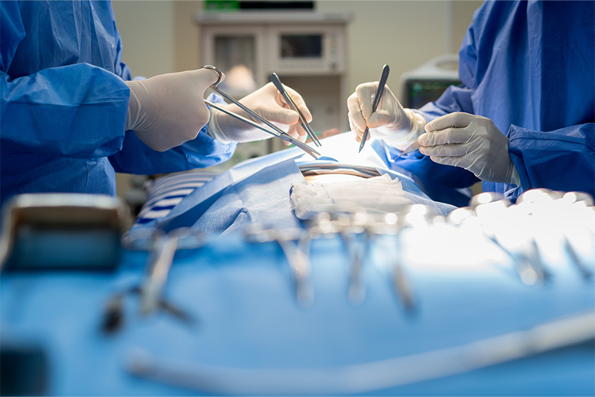 Surgeons wearing gloves and using surgical tools on a patient whose face is not shown.
